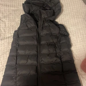 Svart dunväst från Zara - Säljer en svart dunväst från Zara i storlek M. Västen har en dragkedja framtill och en mysig huva. Perfekt för höst och vinter när du vill hålla dig varm men ändå se stilren ut. Passar både till vardags och lite mer avslappnade tillfällen.