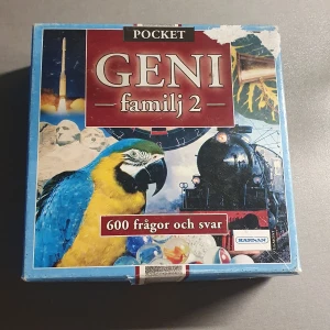 Geni Familj 2 - Säljer ett frågespel från Kärnan, Geni Familj 2. Det är en kompakt pocketversion med 600 frågor och svar. Perfekt för familjekvällar eller att ta med på resan. Omslaget har en färgglad design med en papegoja och ett tåg. Lådan är lite sliten men innehållet är komplett och i bra skick.