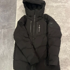 Svart dunjacka från Sail Racing - Säljer en svart dunjacka från Sail Racing i mycket bra skick. Jackan har en praktisk dragkedja och en varm huva, perfekt för kalla vinterdagar. Den är långärmad med justerbara ärmslut för extra komfort. Designad i Sverige och tillverkad i Vietnam. Priset kan diskuteras ordinarie pris 3199kr