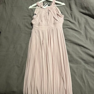 Ljusrosa långklänning - Säljer en superfin ljusrosa långklänning i ett elegant och luftigt material. Klänningen har en halterneck-design och är perfekt för sommarens fester eller bröllop. Den är plisserad och ger en romantisk känsla. Passar perfekt för en speciell kväll! 💖klänningen är från TFNC LONDON och är helt ny med alla lappar kvar💕