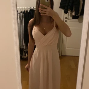 Ljusrosa långklänning med knytband - Säljer en superfin ljusrosa långklänning med smala axelband och omlott-design framtill. Klänningen har ett sött knytband i ryggen som ger en extra touch. Endast använd 2 gånger, och perfekt inför bal eller andra festliga tillfällen.