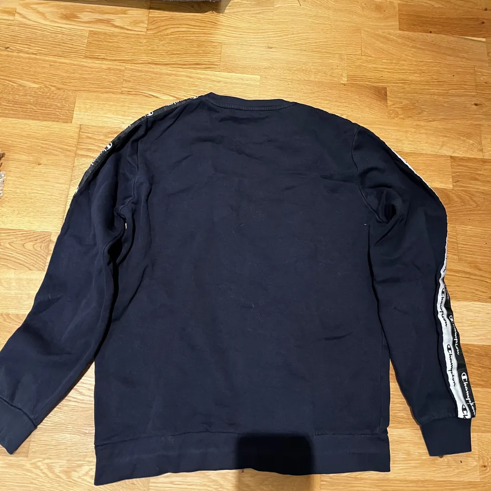 Säljer en snygg mörkblå sweatshirt från Champion i storlek 2X-Large i junior stl .Tröjan har långa ärmar och coola logoband längs ärmarna. Perfekt för en avslappnad stil eller träning. Den är i bra skick och redo för nya äventyr!. Tröjor & Koftor.