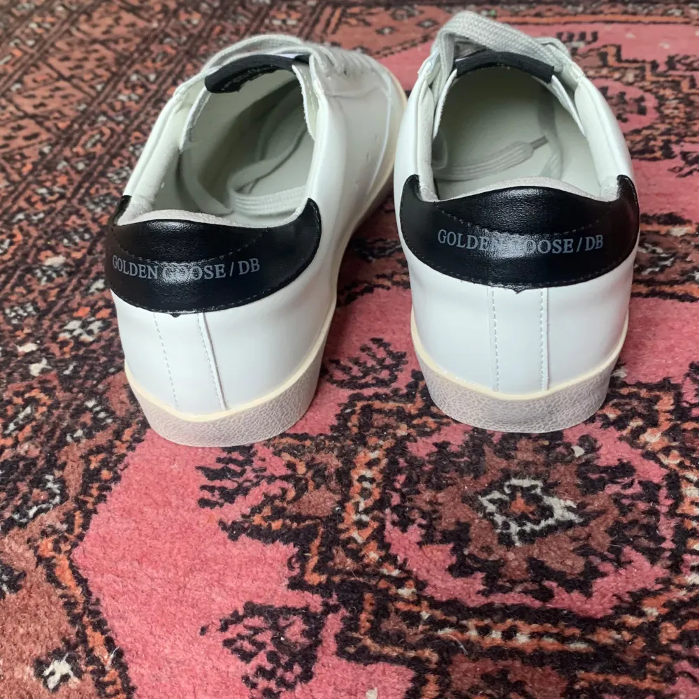 Säljer ett par snygga vita sneakers från Golden Goose med en glittrig stjärna på sidan. Skorna är storlek 40 men passar 39 Skorna har svarta detaljer på hälen och är i mycket bra skick. Perfekta för att ge din outfit lite extra bling! Priset går självklart att förhandlas kom privat för kvitto. Skor.