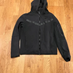 Svart hoodie från Nike - Säljer en svart hoodie från Nike i standard fit. Den har en dragkedja framtill och en huva. Perfekt för höst och vår, och funkar lika bra till träning som till vardags. Den är i bra skick och superbekväm!