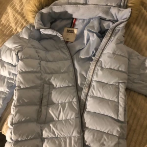 Ljusblå dunjacka från Tommy Hilfiger - Säljer en superfin ljusblå dunjacka från Tommy Hilfiger. Den har en mysig pälskantad huva och dragkedja framtill. Perfekt för kalla vinterdagar! Jackan är i mycket bra skick och håller dig varm och stilren. Passar perfekt till både vardag och festliga tillfällen. Den är egentligen strl L men passar mer M. 