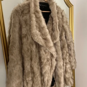 Beige fusk pälsjacka - Säljer en supermysig beige pälsjacka från Zara i mycket bra skick. Perfekt för att hålla sig varm och stilren under höst och vinter. Jackan har en normal passform och långa ärmar, vilket gör den idealisk för både vardag och fest. Den är gjord av syntetmaterial och har en lyxig känsla. Passar perfekt till alla dina outfits!