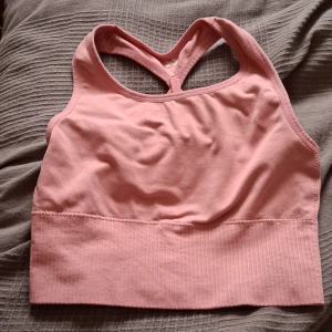 Rosa sport-bh med korsade band - Säljer en rosa sport-bh i mycket bra skick. Den har korsade band i ryggen och en ribbad kant nedtill för extra stöd. Perfekt för träning eller vardagsbruk. Superbekväm och stilren design!