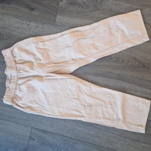 Beige/ gammalrosa linnebyxor med resårmidja för barn. - Säljer ett par bekväma beige/ gammal rosa linnebyxor med resårmidja. Perfekta för en avslappnad stil och passar bra till både vardag och sommaraktiviteter. Byxorna har en loose passform och är i mycket bra skick.