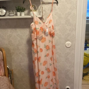 Blommig långklänning med volangdetaljer - Superfin långklänning i ljusrosa med stora blommor. Den har smala axelband och en v-ringad design med volangdetaljer framtill. Den är i storlek M, helt ny!🌸300+ frakt