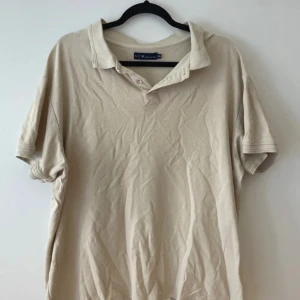 Beige pikétröja från S.C.W. - Säljer en klassisk beige pikétröja från S.C.W. i storlek XXL. Tröjan har en krage med knappar och korta ärmar, perfekt för en avslappnad stil. Passar bra till både vardag och lite finare tillfällen. Skön och enkel att matcha med det mesta i garderoben.