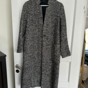 Svartvit kappa från Zara Basic - Säljer en stilren svartvit kappa från Zara Basic i mycket bra skick. Den har ett klassiskt mönster och är perfekt för höst och vår. Kappan har långa ärmar och stängs med en knapp framtill. Superfin att ha både till vardags och fest!