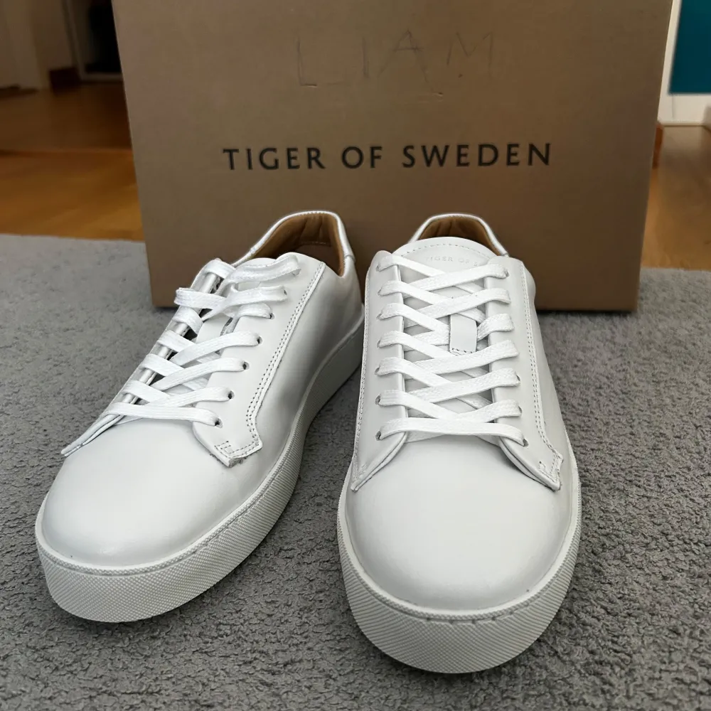 Säljer ett par stilrena vita sneakers från Tiger of Sweden i skinn. De har en klassisk design med snörning och en bekväm passform. Perfekta för både vardag och festliga tillfällen. Skorna är i nytt skick och kommer i originalförpackning. Ifall frågar så är det bara att skicka ett meddelande. . Skor.