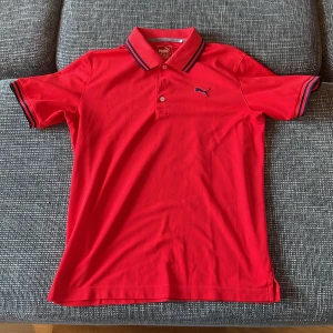 Röd pikétröja från Puma - Säljer en snygg röd pikétröja från Puma i mycket bra skick. Tröjan har korta ärmar och en klassisk krage med mörkblå ränder. Perfekt för både vardag och sportiga aktiviteter. Puma-loggan är broderad på bröstet. Passar perfekt till sommaren! 🌞pris kan alltid förhandlas!