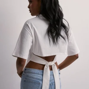 Vit kortärmad topp med knytband - Säljer en superfin vit topp med korta ärmar och knytband i ryggen. Perfekt för sommardagar eller en avslappnad utekväll. Toppen har en tight passform och är gjord i ett mjukt material som känns skönt mot huden. Ingen lapp kvar men har endast använt den 2 - 4 gånger. 