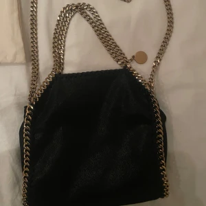 Stella McCartney väska - Super fin Stella McCartney väska i modellen falabella tiny tote - svart med guld detaljer,  fint skick och äkthetsbevis finns! Lite guld har släppt på kedjan men inget som märks mycket!