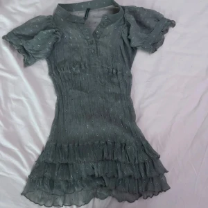 Grön kort klänning/topp från Naf Naf - Söt grå klänning från Naf Naf med korta puffärmar och volangdetaljer. Den har ett diskret prickigt mönster och knappar framtill. Perfekt för vår och sommar💚❤️‍🔥💝