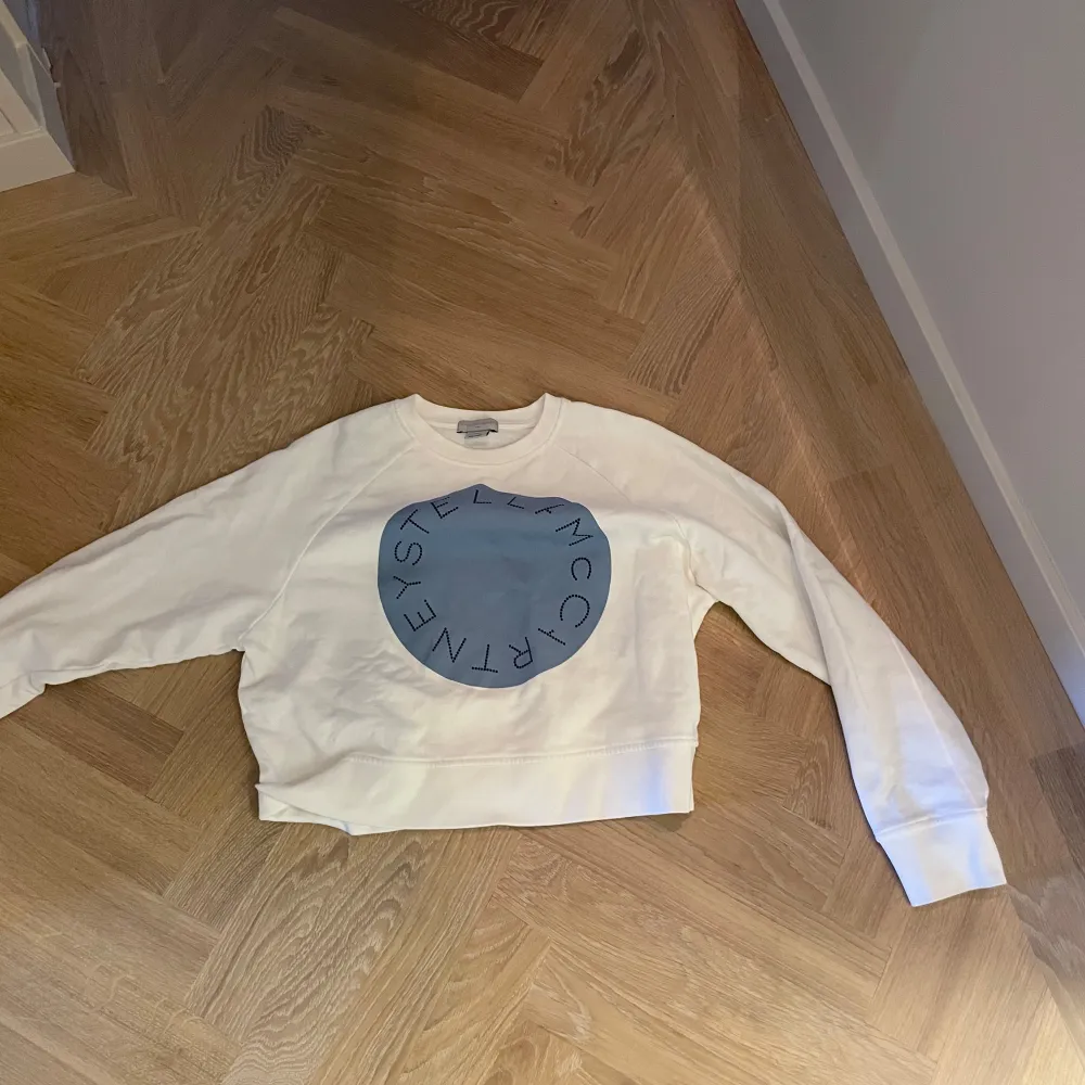 Säljer en superfin vit tröja från Stella McCartney Kids. Den har ett stort blått tryck på framsidan med text. Tröjan är i bra skick och perfekt för både vår och höst. Den är långärmad och gjord i ett mjukt material som känns skönt mot huden.. Tröjor & Koftor.