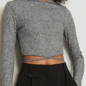 Grå croppad topp - Säljer min gråa topp med långa ärmar och croppad passform. Den har en knytning runt midjan som ger en extra detalj. Perfekt för både vardag och fest.