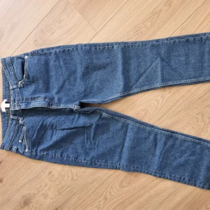 Blå jeans från H&M - Säljer ett par klassiska blå jeans från H&M. De har en straight passform och är tillverkade i ett slitstarkt denimtyg. Perfekta för vardagsbruk och kan enkelt matchas med olika toppar. De har fickor både fram och bak samt en traditionell dragkedja och knapp framtill.