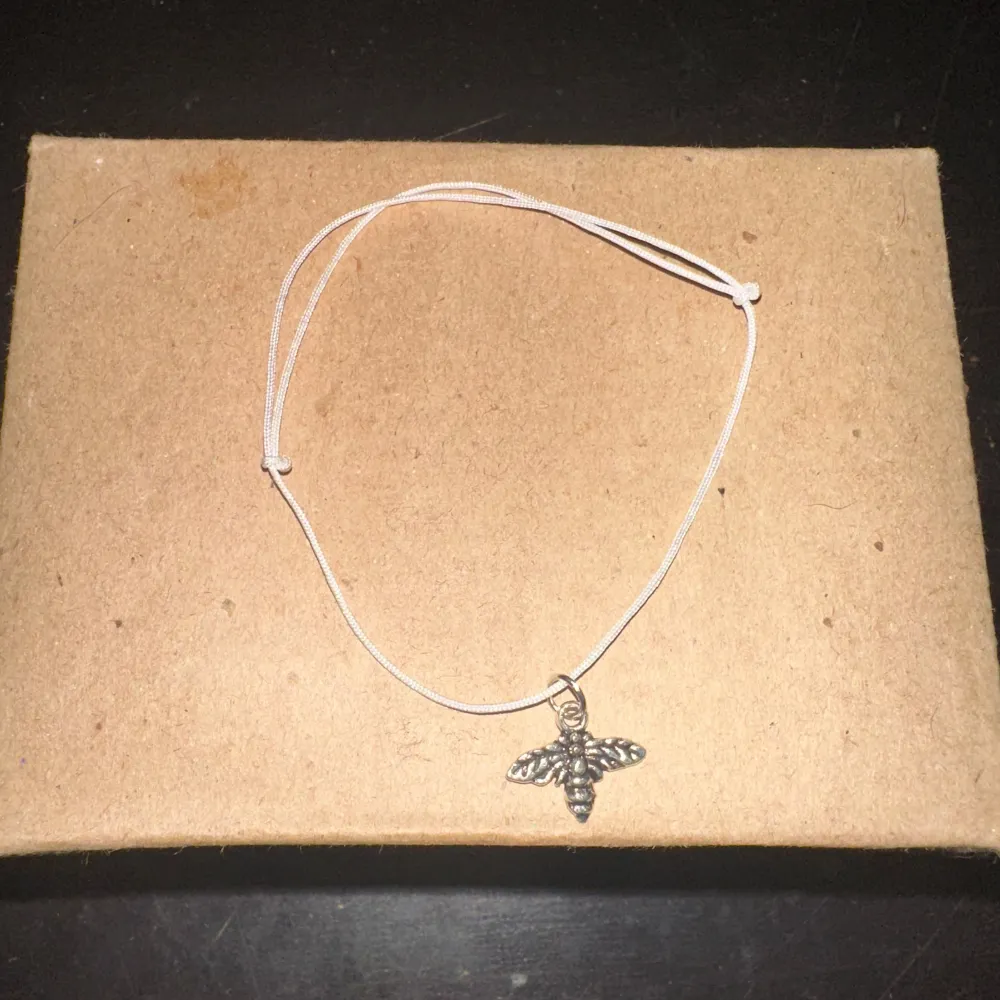 Säljer ett enkelt och stilrent armband med en söt bi-berlock. Armbandet har en tunn vit tråd som ger en minimalistisk look. Perfekt för vardagsbruk eller som en subtil accessoar till festligare tillfällen.. Asusteet.