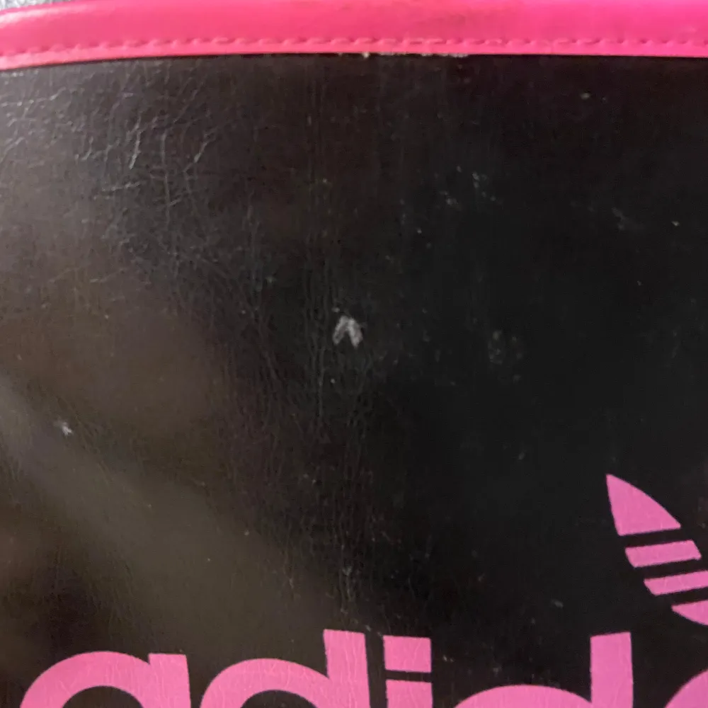 Säljer en cool svart axelväska från Adidas med rosa detaljer och logga. Väskan har en justerbar axelrem och en praktisk dragkedja upptill. Perfekt för att bära med sig det viktigaste när du är på språng. Lite slitage syns på ytan, men den är fortfarande i bra skick.. Väskor.