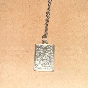 Silverfärgat halsband med rektangulär berlock - Säljer ett coolt silverfärgat halsband med en rektangulär berlock. Berlocken har ett detaljerat motiv ”the star” tarotkort. Kedjan är i en enkel och stilren design. Perfekt för att ge en unik touch till din outfit!