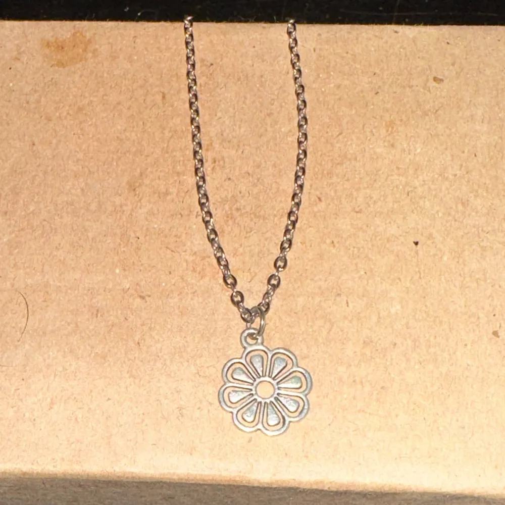 Säljer ett superfint silverfärgat halsband med en blomformad berlock. Kedjan är enkel och stilren, perfekt för både vardag och fest. Blomman har en öppen design som ger en lätt och luftig känsla. Passar perfekt som en söt detalj till din outfit!. Asusteet.