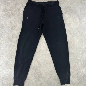 Svarta mjukisbyxor från Maya Delorez - Säljer ett par svarta mjukisbyxor från Maya Delorez. De är superbekväma med elastisk midja och snörning. Byxorna har en stilren design med gråa detaljer längs sidorna där det står 'Maya Delorez'. Perfekta byxor för mysiga dagar hemma eller i stallet.