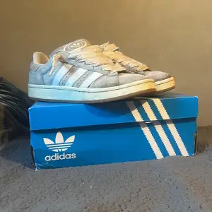 Säljer ett par gråa Adidas Campus 00s sneakers i storlek herr 43. Skorna är i en snygg grå färg med vita detaljer och klassiska tre ränder på sidan. De är i bra skick och kommer med originalkartong. Perfekta för både vardag och fest!