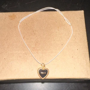 Armband med hjärthänge - Säljer ett sött armband med ett hjärthänge. Hänget är guldigt med en svart insida där det står 'love'. Bandet är tunnt och enkelt, perfekt för att bära till vardags eller på fest.