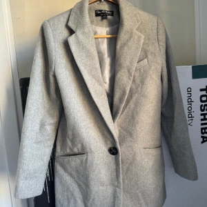 Grå kavaj från Miss Selfridge - Säljer en stilren grå kavaj från Miss Selfridge. Den har en klassisk design med en knapp framtill och är perfekt för både vardag och fest. Kavajen är tillverkad i ett mjukt material och har en snygg passform.