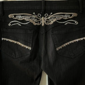 Lågmidjade svarta y2k jeans - Supersnygga lågmidjade svarta bootcut jeans med gulligt brodyr där bak💞Säljer därav de har knappt kommit till användning. Midjemåttet tvärs över är 37/38 cm och längden är 103cm, skriv privat om du har några frågor💗Priset går att diskutera🤍