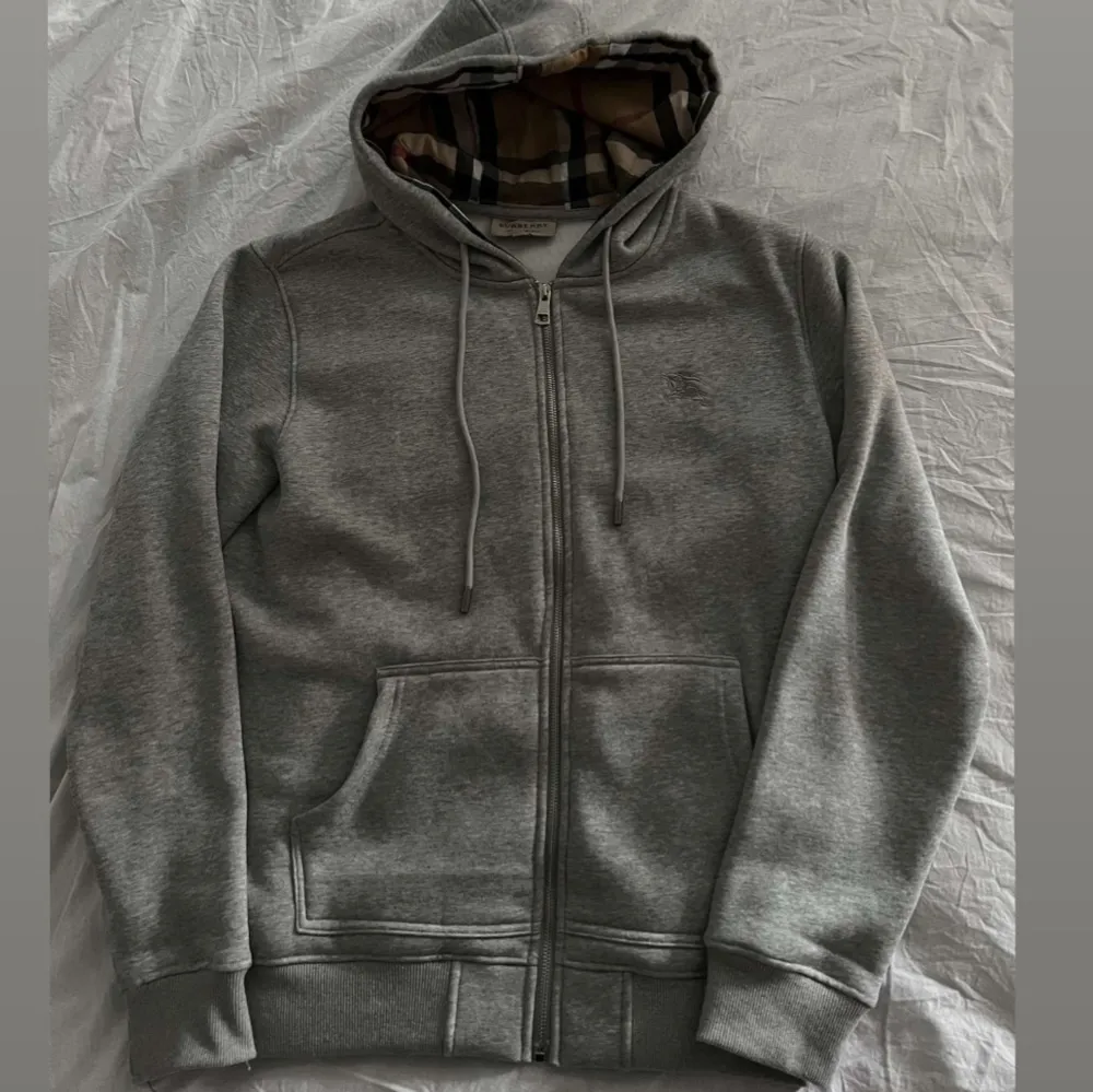 Säljer en snygg grå hoodie från Burberry. Den har en klassisk dragkedja och en cool fodrad huva med det ikoniska Burberry-mönstret. . Tröjor & Koftor.