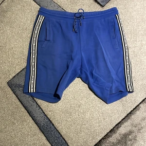 Blå shorts från Michael Kors - Säljer ett par snygga blå shorts från Michael Kors. De har en stilren design med vita och svarta ränder längs sidorna och en praktisk dragsko i midjan. Fint skick! Ord pris 1499 Mitt pris: 850