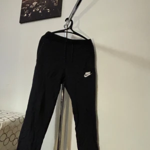 Svarta mjukisbyxor från Nike - Säljer ett par svarta mjukisbyxor från Nike i storlek S. Byxorna har en bekväm passform med snörning i midjan och det klassiska Nike-loggan på benet. Perfekta för träning eller en avslappnad dag hemma. Har använt dessa En gång!!! Nypris: 599kr