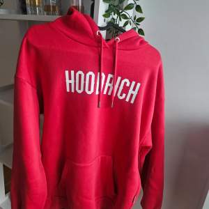 Säljer en snygg röd hoodie från Hoodrich. Den har en stor, bekväm huva och en praktisk magficka. Perfekt för en avslappnad stil och passar bra till både vardag och chill. Texten 'Hoodrich' står i vitt på framsidan. Grym för höst och vinter!