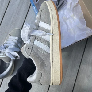 Adidas Campus 00s grey - Gråa Adidas Campus 00s    Använda i nästan en säsong. Ganska bra skick. Ett par mörkgråa skosnören och skokartong ingår. Köpta på Merch Sweden hemsida. Nypris: 1 599kr  Strl. 39 1/3