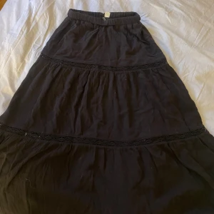 Svart långkjol från H&M Divided - Säljer en superfin svart långkjol från H&M Divided. Kjolen har en elastisk midja och är dekorerad med snygga spetsdetaljer som ger den en extra touch. Perfekt för både vardag och fest! 🖤