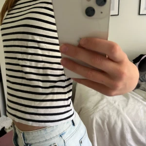 Randig croppad topp - Säljer en superfin randig topp i svart och vit. Den är croppad och har korta ärmar, perfekt för sommaren. Toppen är i bomull och känns väldigt skön mot huden. Passar både till jeans och kjol för en avslappnad look.🥰
