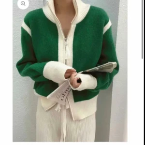 Grön och vit stickad kofta - Säljer en superfin grön och vit stickad kofta med dragkedja. Den har långa ärmar och en mysig, oversized passform. Perfekt för höst och vinter när du vill hålla dig varm och stilren. Koftan har vita detaljer vid ärmslut och krage som ger en snygg kontrast.