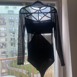 Svart långärmad body från Amisu - Säljer en supercool svart body från Amisu i storlek M. Den har ett unikt mesh-tyg med långa ärmar och en tight passform. Perfekt för en utekväll eller fest! 🖤