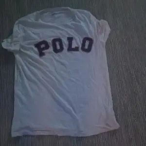 Säljer en vit t-shirt från Polo med stora bokstäver i mörk färg på framsidan. Den är kortärmad och perfekt för en avslappnad stil. Passar bra till jeans eller shorts för en cool vardagslook.