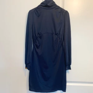 Mörkblå klänning från Chiara Forthi - Säljer en elegant mörkblå gravidklänning från Chiara Forthi. Den har långa ärmar och en hög krage som ger en stilren look. Perfekt för höst- och vinterevenemang. Klänningen är i nyskick och har en fin passform som framhäver figuren.