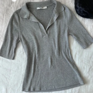 Grå ribbad topp från NA-KD - Säljer en snygg grå ribbad topp från NA-KD i storlek M. Den har en stilren krage och trekvartsärmar, perfekt för både vardag och lite finare tillfällen. Toppen är i ett mjukt och bekvämt material som sitter skönt på kroppen.