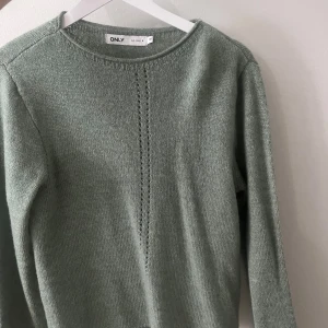 Stickad grön tröja - Tunn stickad grön tröja med fina detaljer på framsidan! Har inte används någon gång. Köpt för länge sedan!