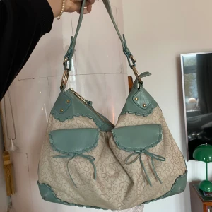Beige och grön axelväska - Säljer en superfin axelväska från DKNY i beige och grön färg💞Perfekt för vardagsbruk och rymmer allt du behöver! Är sliten på undersidan av väskan (se bild 4&5) men annars i fint skick!💓💓