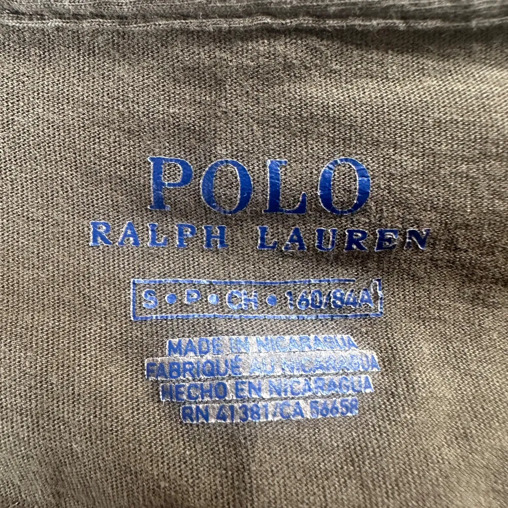 Säljer en snygg olivgrön t-shirt från Ralph Lauren. Den har en v-ringad hals och korta ärmar, perfekt för en avslappnad stil. T-shirten är i bomull och har en liten broderad logga på bröstet. Passar både till vardags och lite finare tillfällen.. T-shirts.