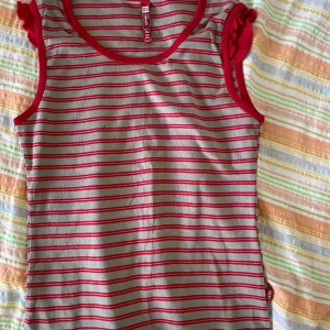 Randig ärmlös topp från C&A - Säljer en söt randig topp från C&A i storlek XS. Den är ärmlös med röda och vita ränder och har en bekväm passform. Perfekt för sommardagar eller som ett lager under en kofta. Toppen är i bra skick med en liten fläck på framsidan.