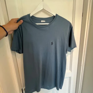 Blå t-shirt från Ralph Lauren - Säljer en snygg blå t-shirt från Ralph Lauren. Den har en klassisk passform och är gjord i mjuk bomull. Perfekt för vardagsbruk eller en avslappnad dag ute. Den har en liten broderad logga på bröstet.