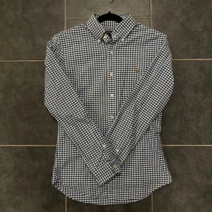 Rutig skjorta från Ralph Lauren - Snygg rutig skjorta från Ralph Lauren i blått och vitt. Skjortan har långa ärmar och klassiska knappar framtill. Den är broderad med den ikoniska loggan på bröstet. Perfekt för en stilren look!